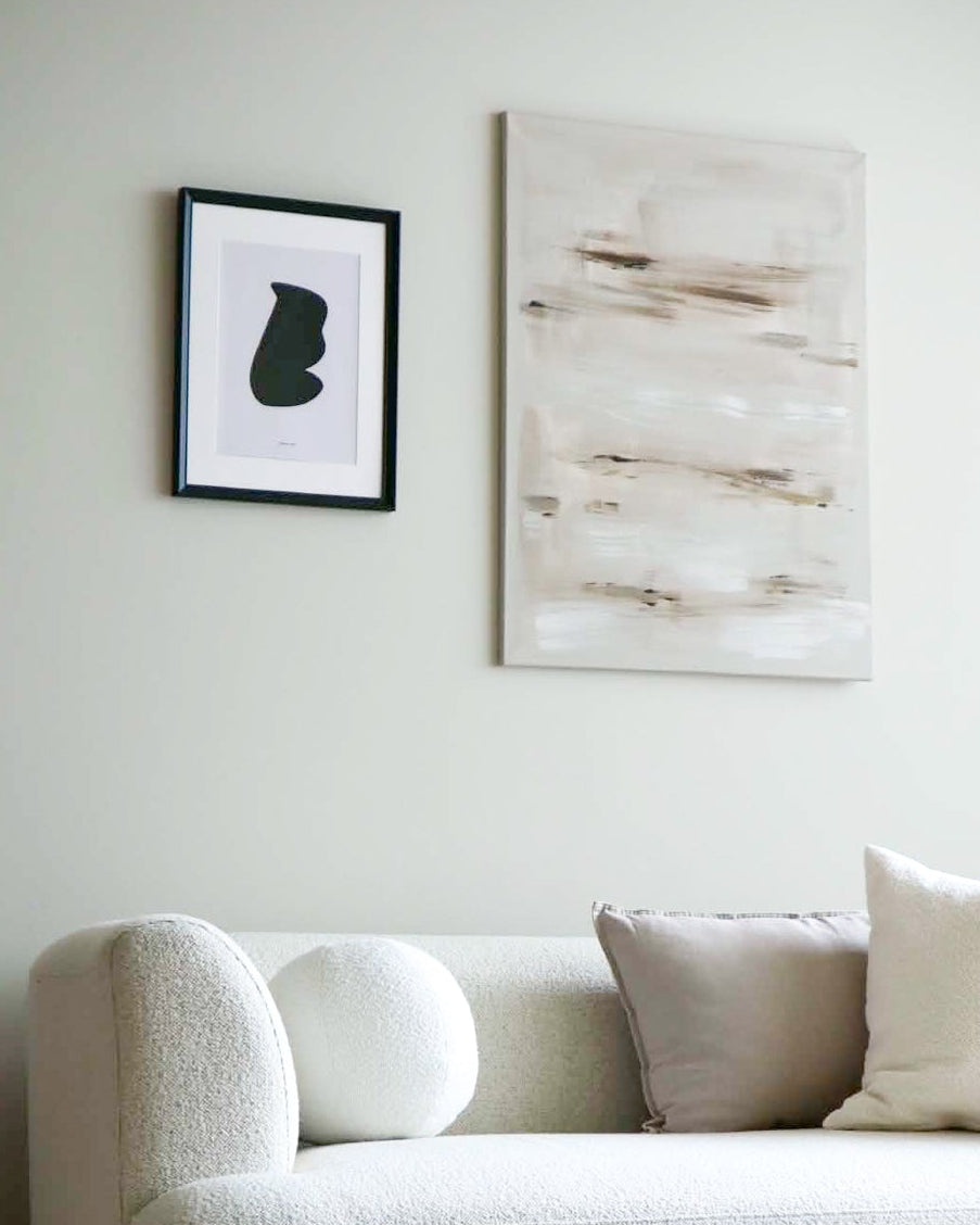 A modern living room corner featuring a textured off-white boucle sofa with neutral throw pillows, a round wooden coffee table, and minimalist wall art on a light gray wall.